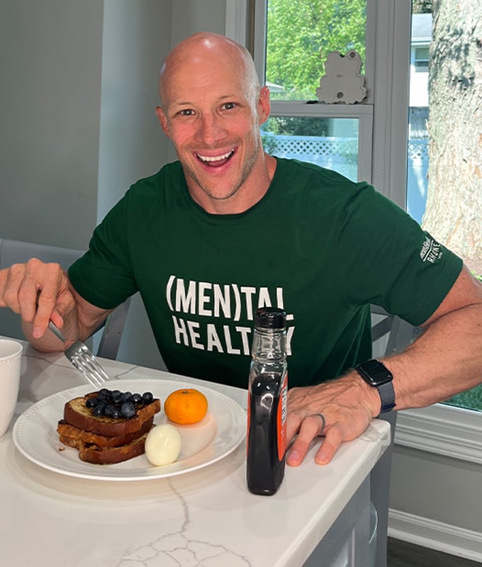 Coach is smiling and having a plate with three toasts, bluberries, one egg, one tangerine and syrup on the side